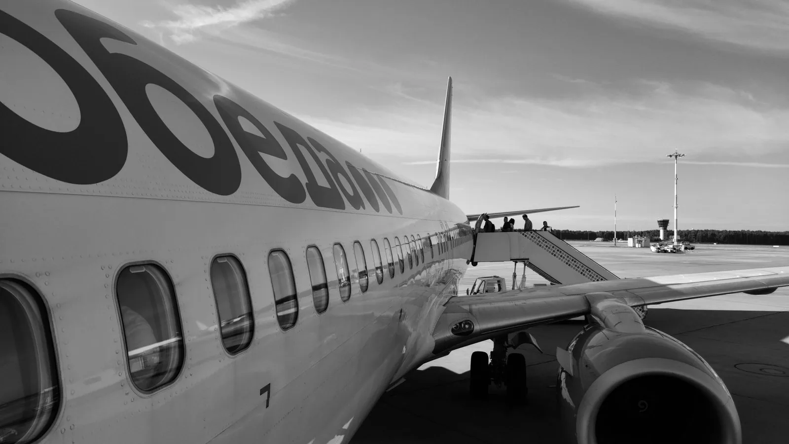 Monochrome image of an airplane on the tarmac with passengers boarding via stairs.