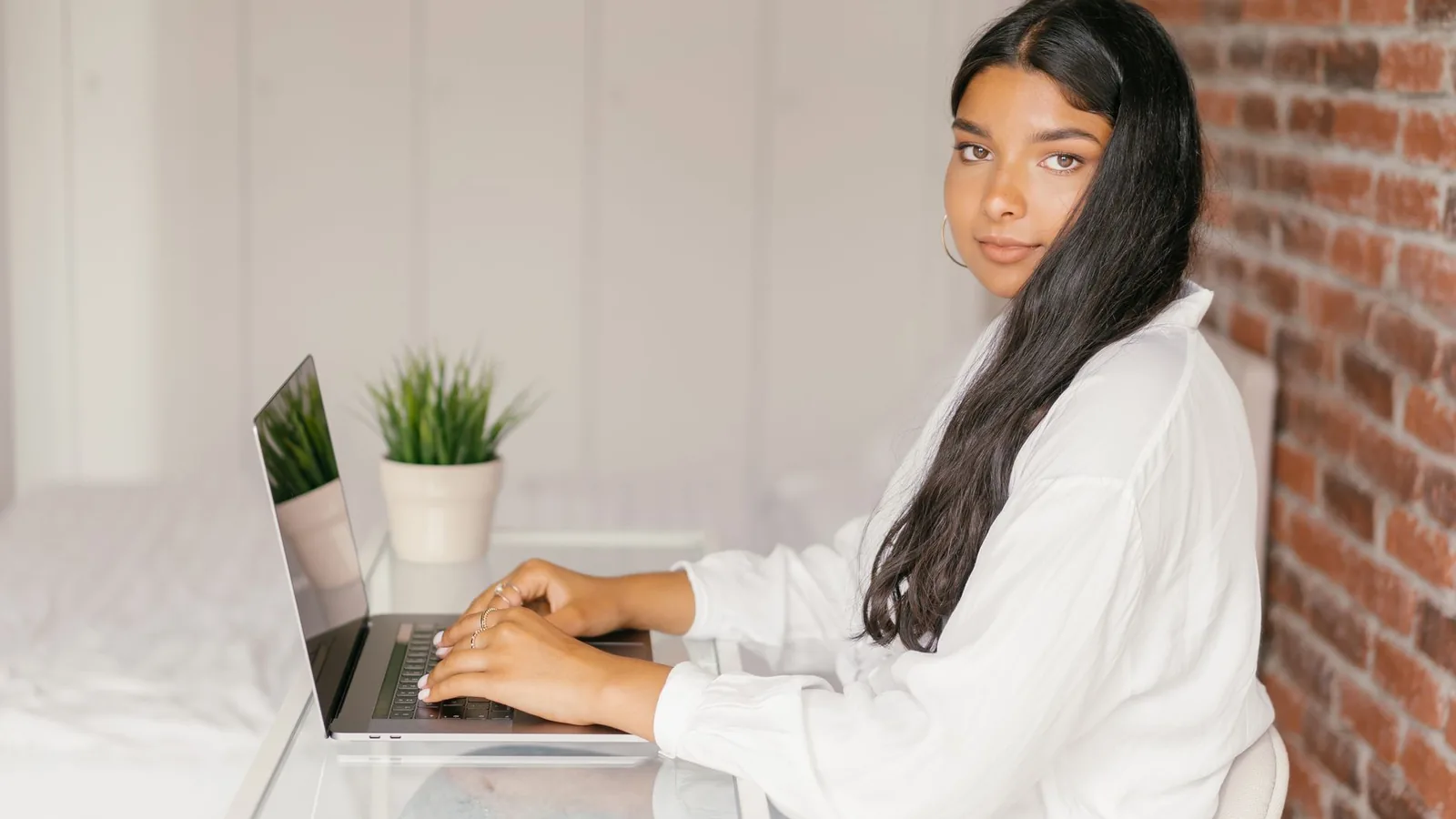 A young woman sits at a desk working on a laptop in her home office.