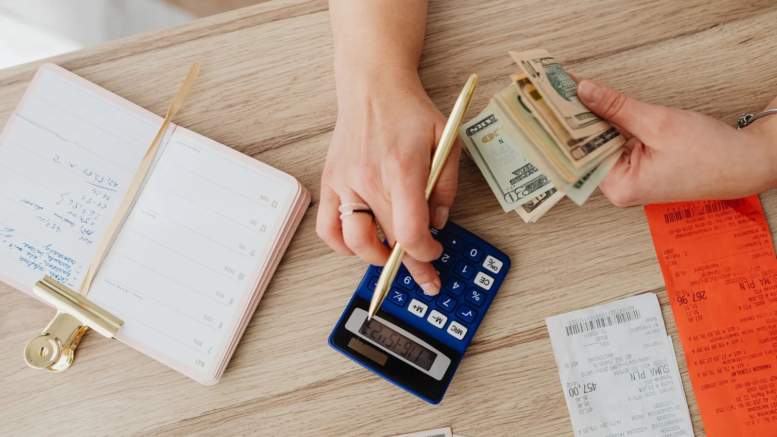 Hands managing finances with calculator, cash, and receipts on a wooden table. Ideal for budgeting concepts.
