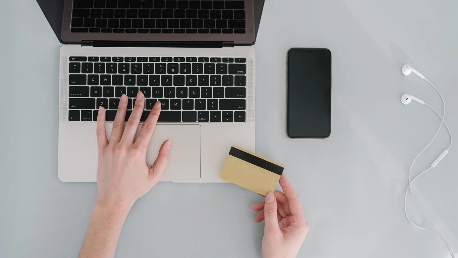 Flat lay of a workspace with a laptop, bank card, smartphone, and earphones, ideal for online finance themes.