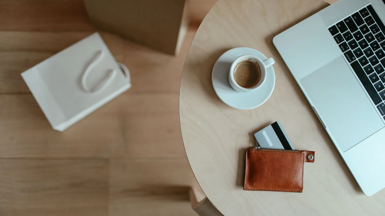 Minimalist top view of a workspace with coffee, laptop, and wallet on a wooden table.