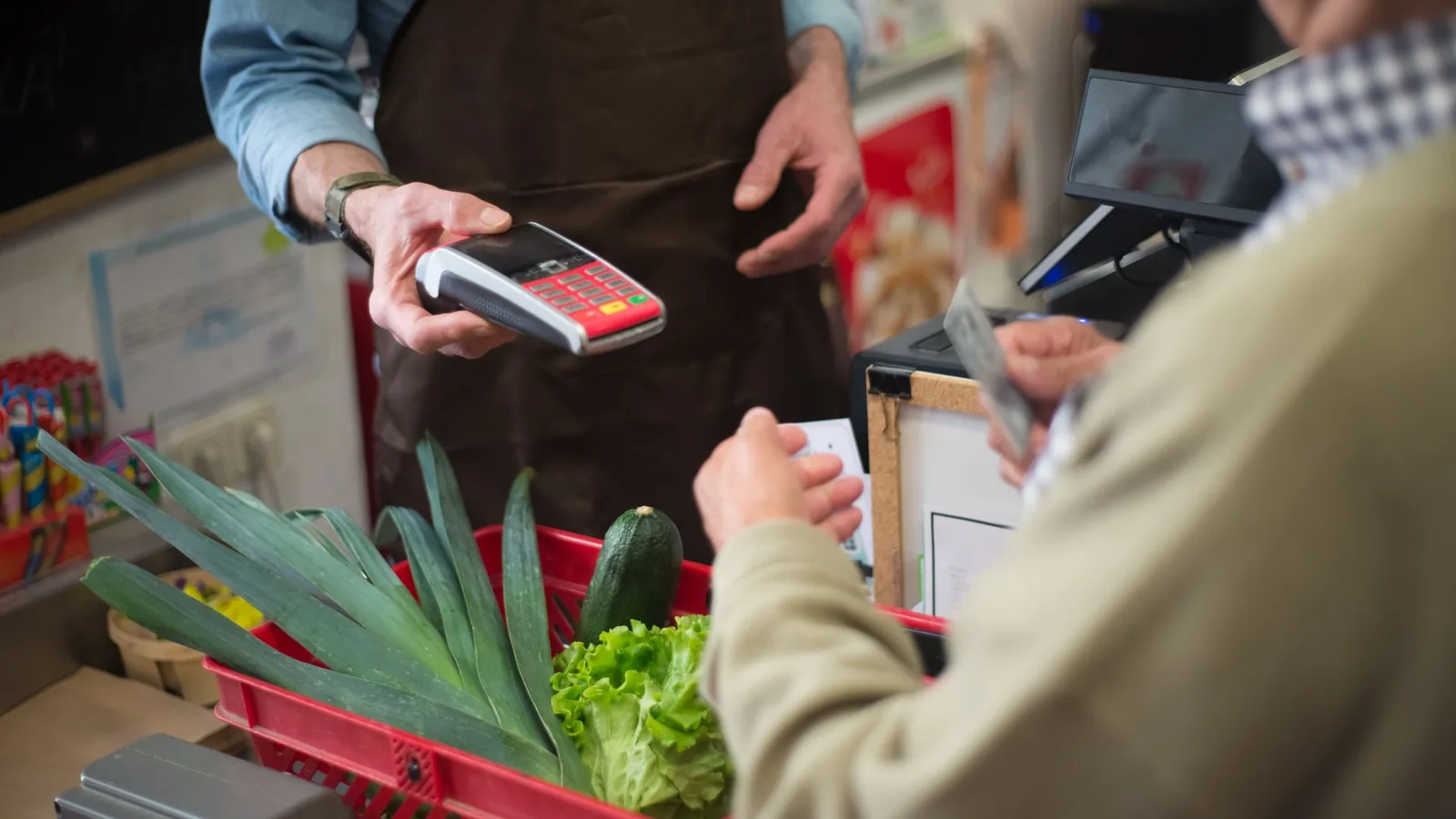 Close-up of customer paying for groceries with produce at a store checkout counter.