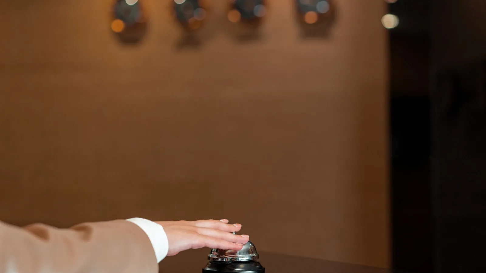 A hand pressing a bell at a hotel reception, symbolizing service and hospitality.