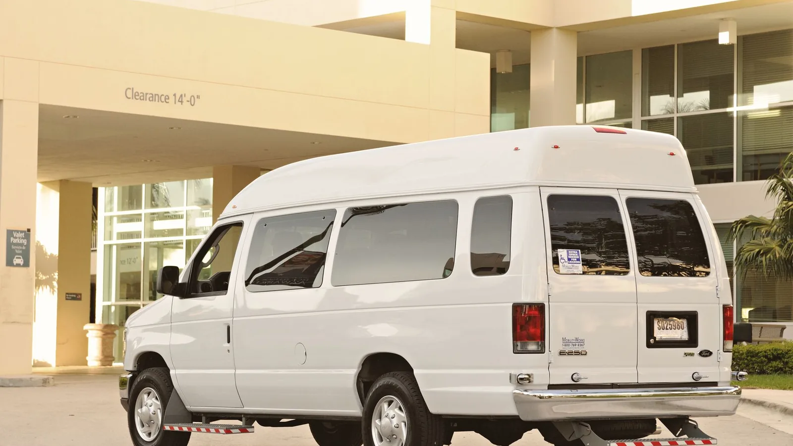 A large white passenger van parked in front of a modern office building entrance.