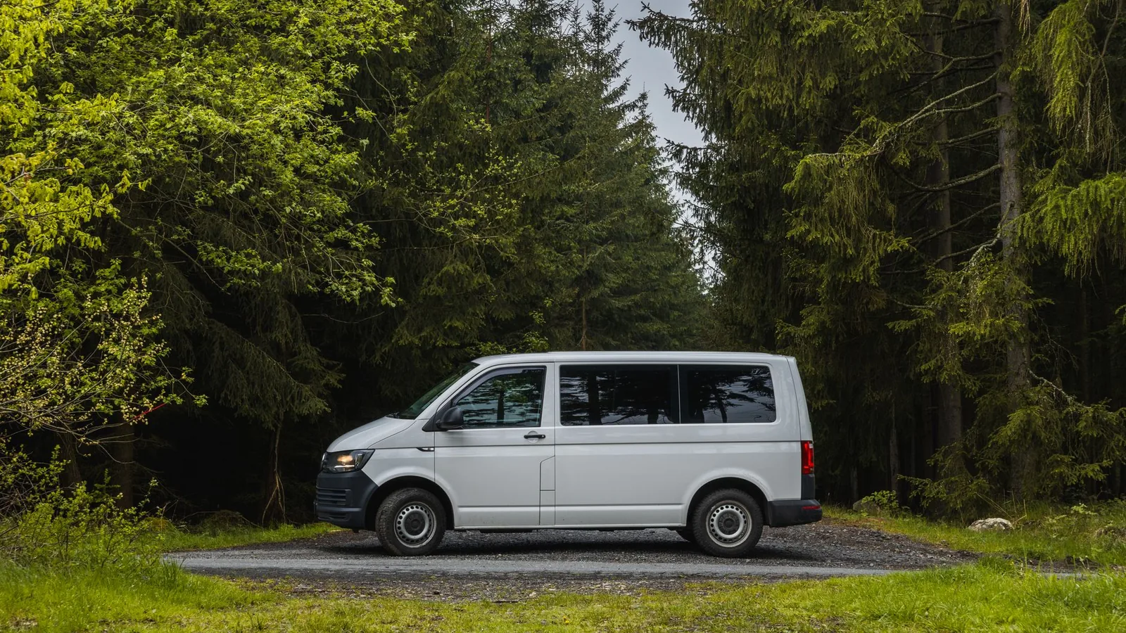 A white van is parked on a gravel road surrounded by dense trees in a tranquil forest setting.