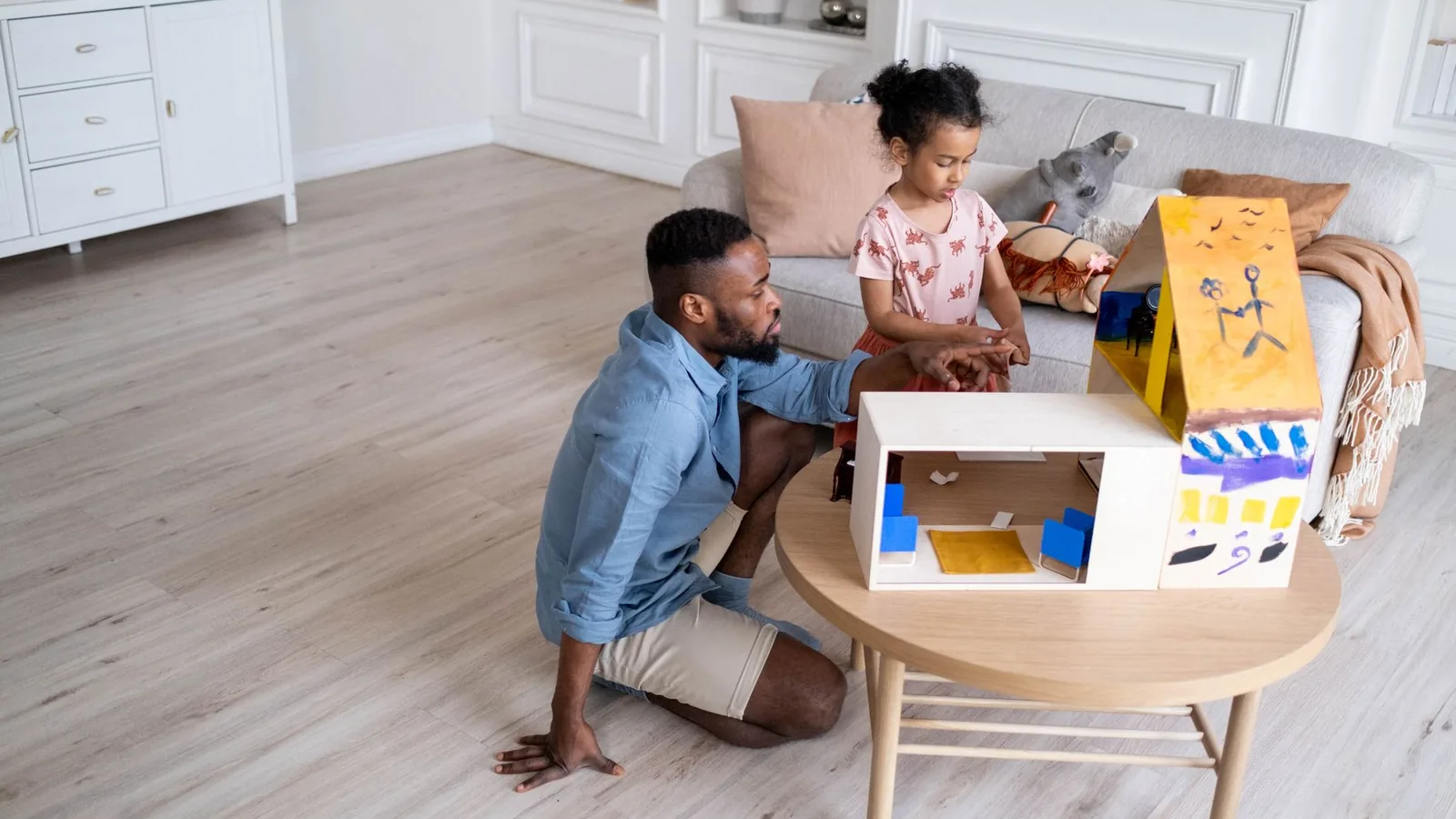A charming family moment as a father and daughter engage with a dollhouse in their living room.