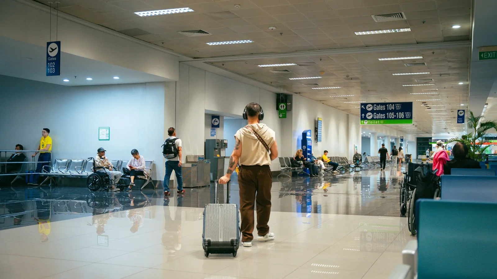 Passengers in a spacious airport terminal, some seated and others walking.
