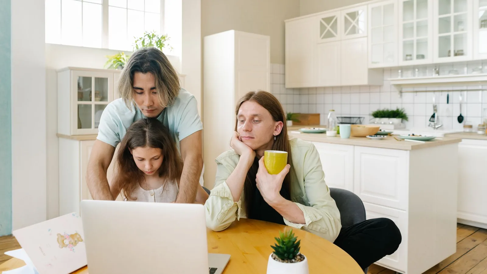 A family spends quality time together in a modern kitchen, focused on a laptop.
