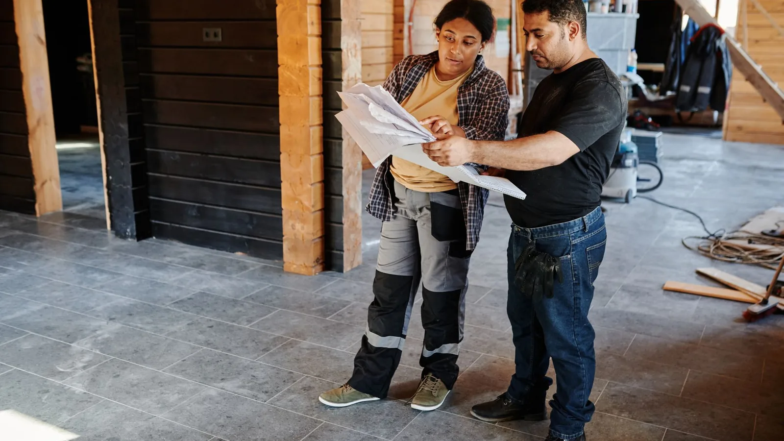 Two workers examining blueprints inside a building under construction, showcasing teamwork.