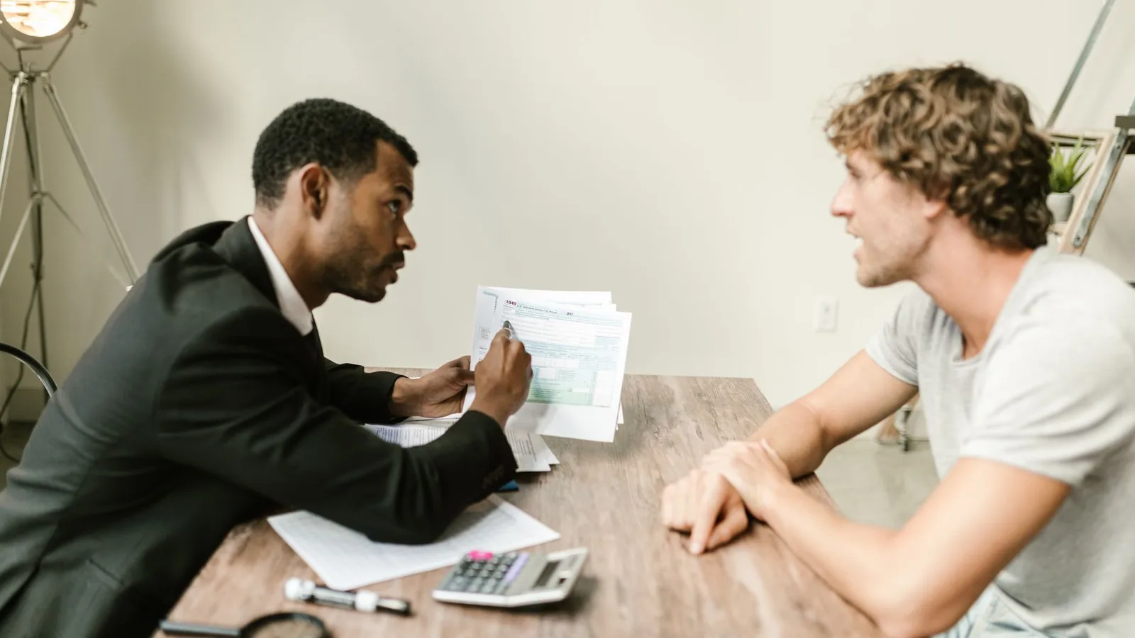 A financial advisor discusses paperwork with a client at a desk in a modern office.