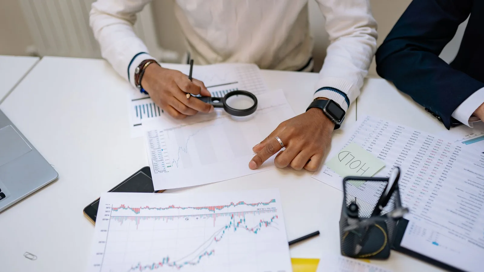 Business professionals reviewing charts with a magnifying glass in an office setting.