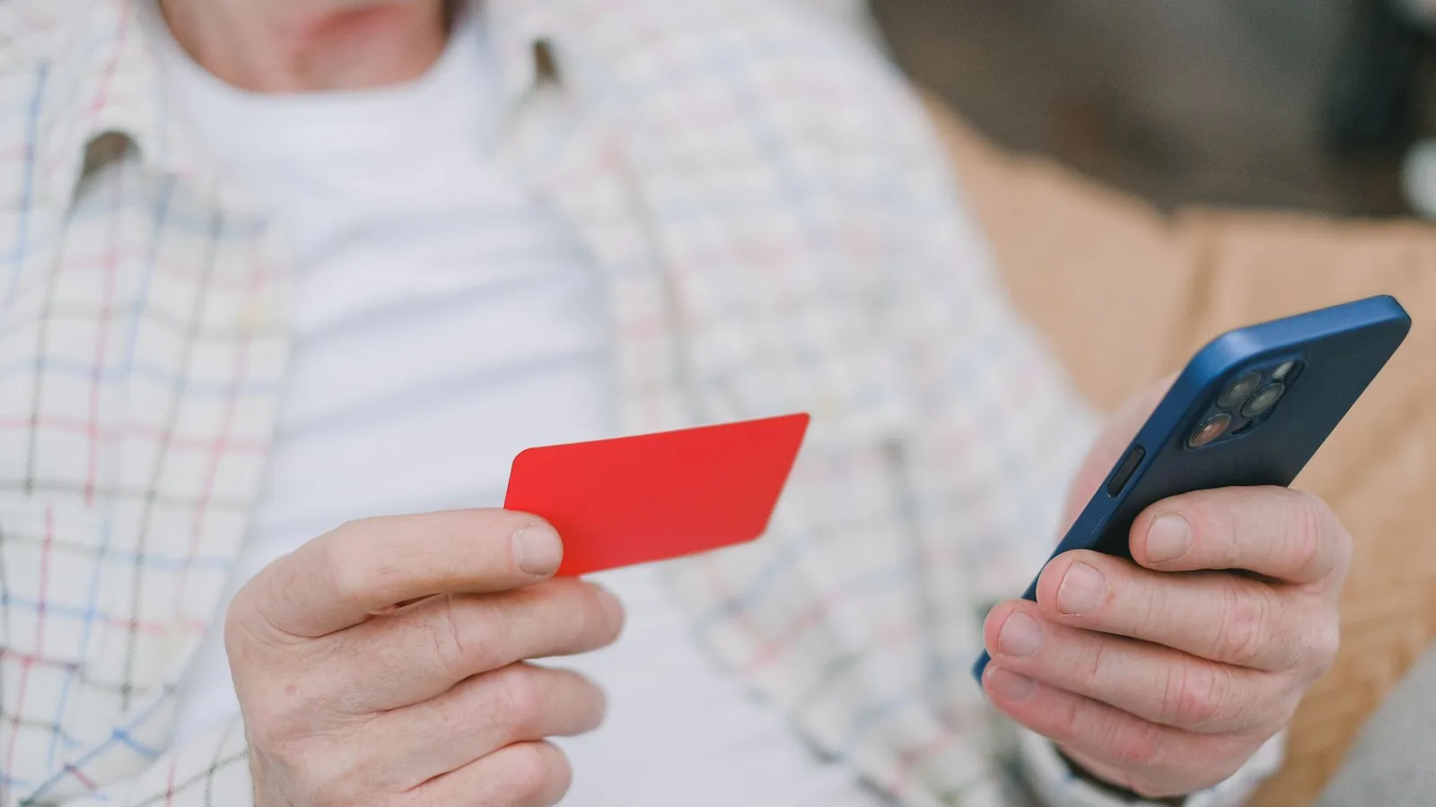 Close-up of a senior adult handling a card and smartphone for online payment.