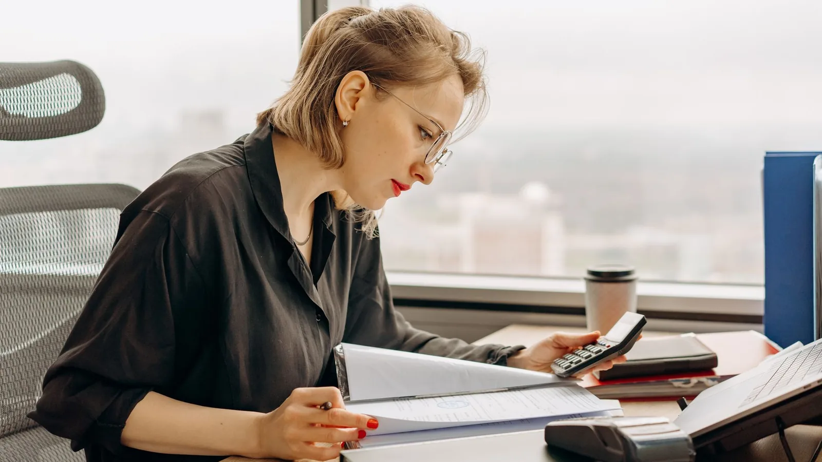 Woman accountant calculating financial documents at office desk.