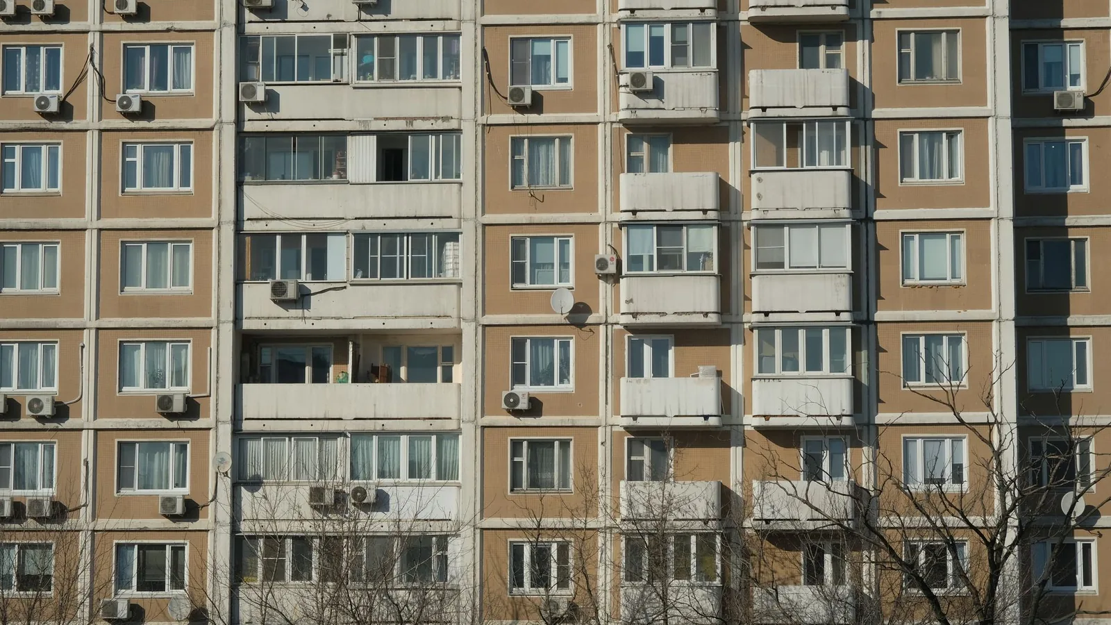 Front view of a sunlit urban apartment building with balconies and air conditioning units.