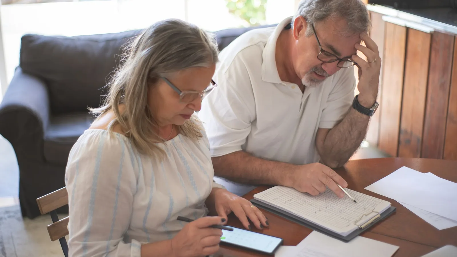 Elderly couple reviewing bills and documents at home, focusing on finances and technology.