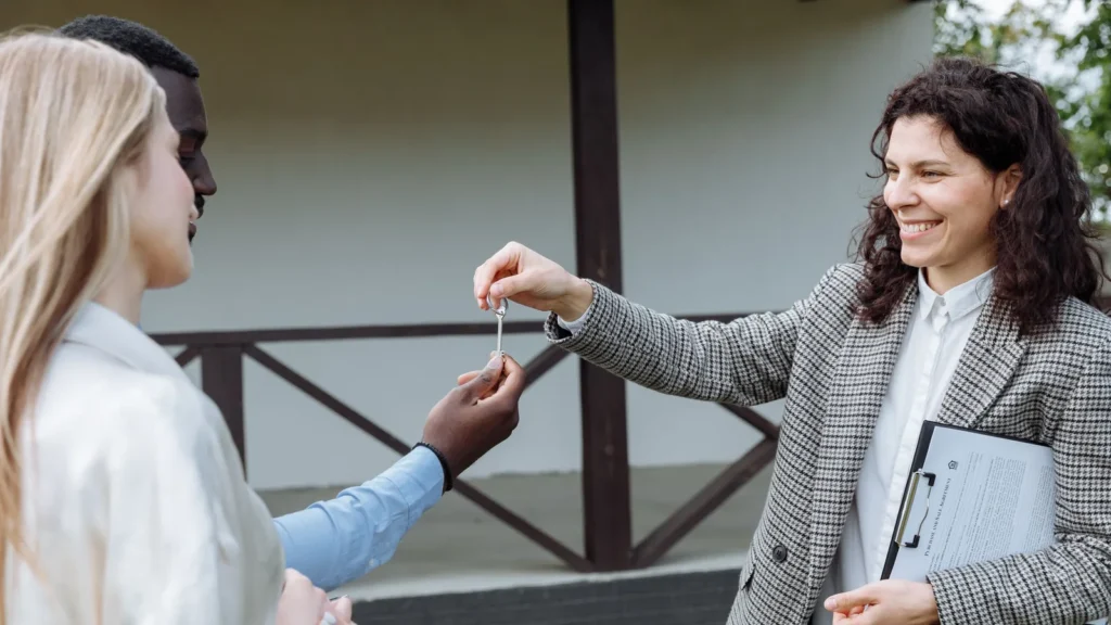 A real estate agent handing house keys to a couple outside their new home