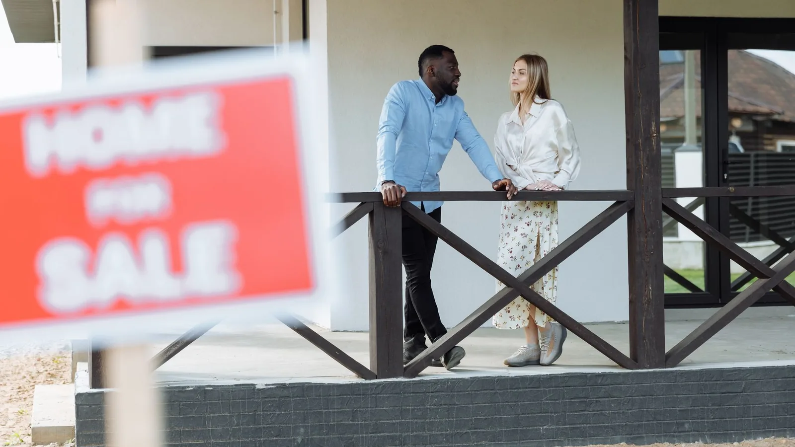A black man and caucasian woman discussing a property for sale on a porch. Ideal for real estate content.