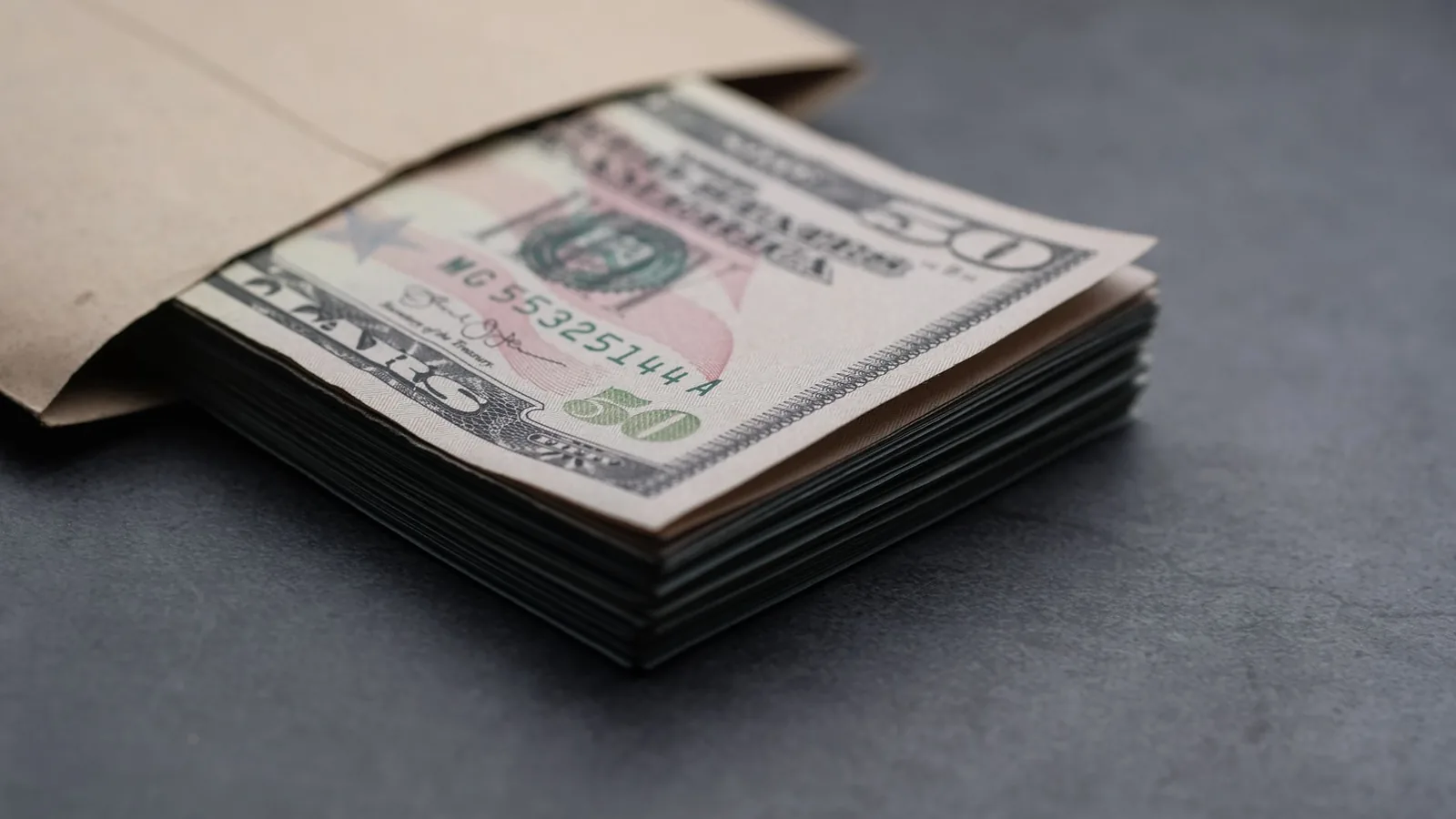 Close-up of US fifty dollar bills partially enclosed in a brown envelope, symbolizing finances.