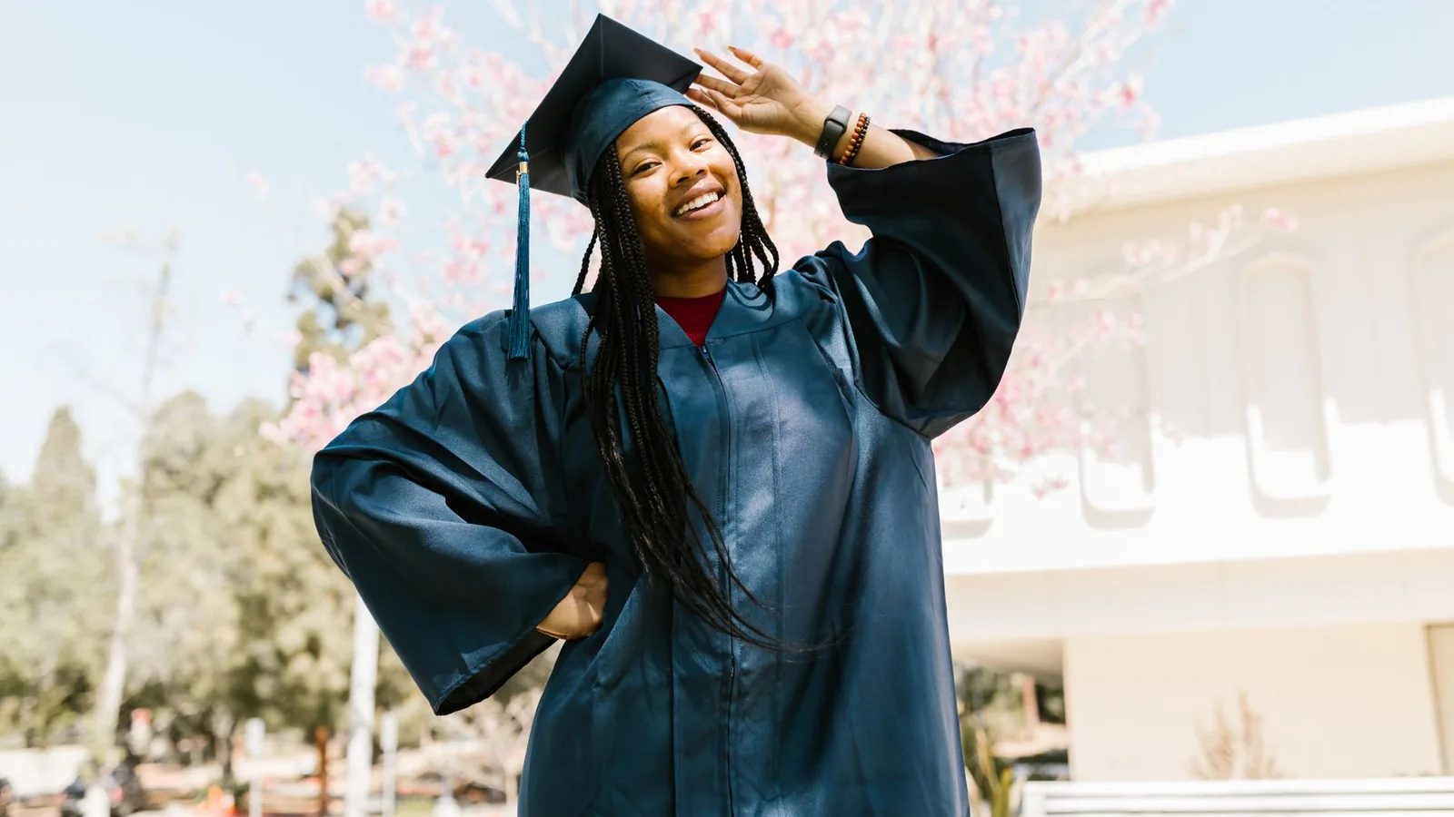 A joyful graduate poses outdoors in a blue cap and gown, celebrating success.