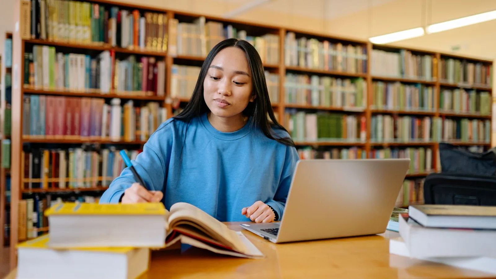Young woman studying in a library with books and laptop, focusing on education.