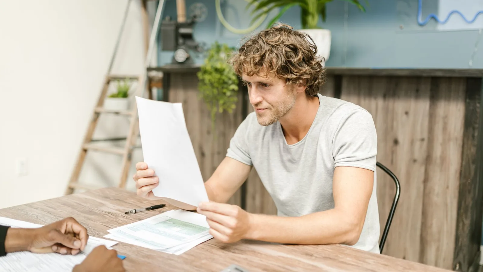 A man with curly hair evaluates documents at a desk, highlighting focused work in a professional setting.
