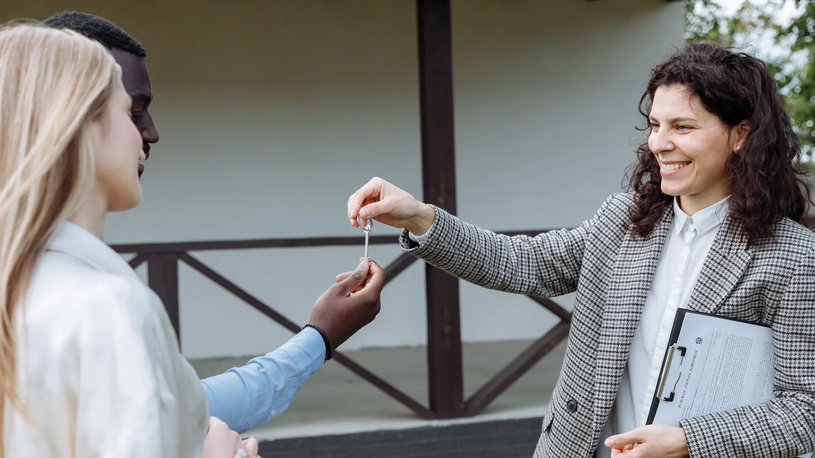 A real estate agent handing house keys to a couple outside their new home